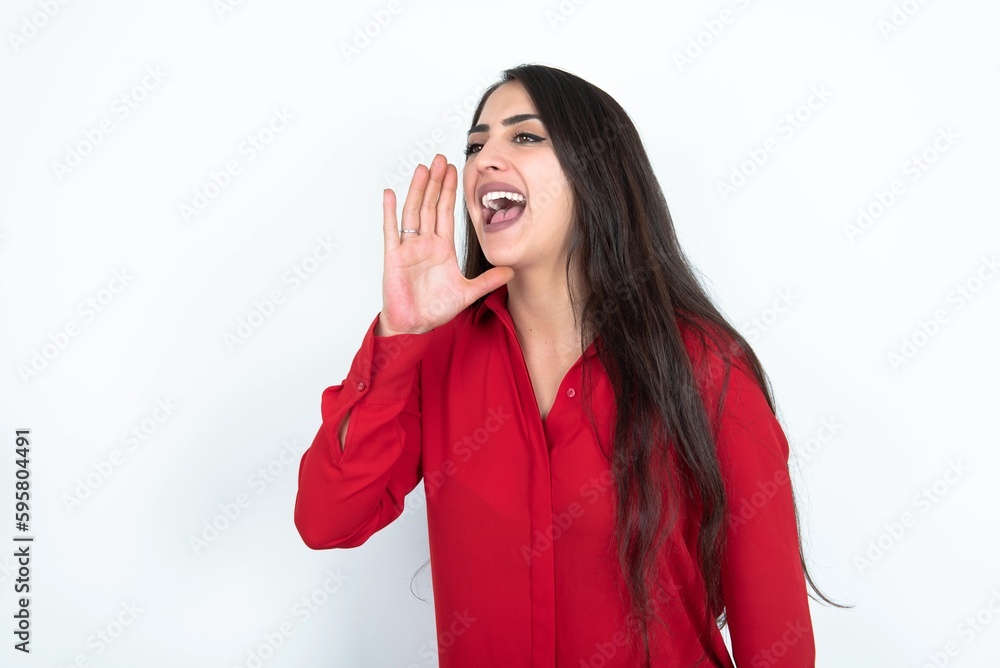 Young brunette woman wearing red shirt over white studio background look empty space holding hand face and screaming or calling someone. Young brunette woman wearing red shirt over white studio background look empty space holding hand face and screaming or calling someone.