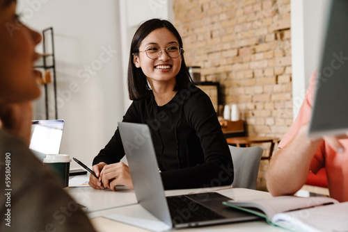 Asian woman smiling while sitting at table with her colleagues during meeting in office photo