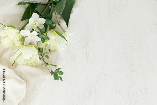 Happy Mothers day. Beautiful white tulips and daffodils on soft fabric on rustic wooden table flat lay with space for text. Stylish spring bouquet from garden. Womens day