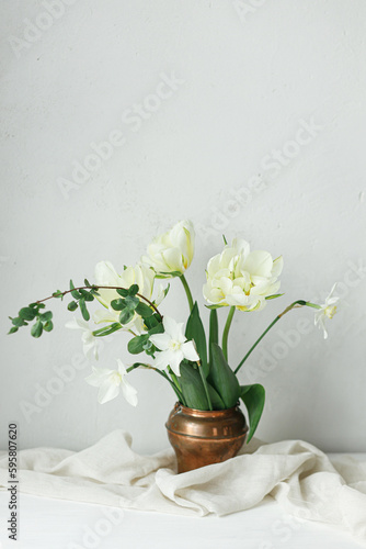 Happy Mothers day. Beautiful white tulips and daffodils in vintage vase on wooden table against rustic wall. Stylish simple spring bouquet, floral still life. Womens day. Space for text