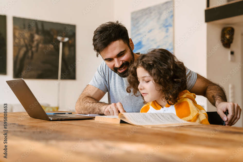 Father smiling while helping his son with homework sitting at table ...