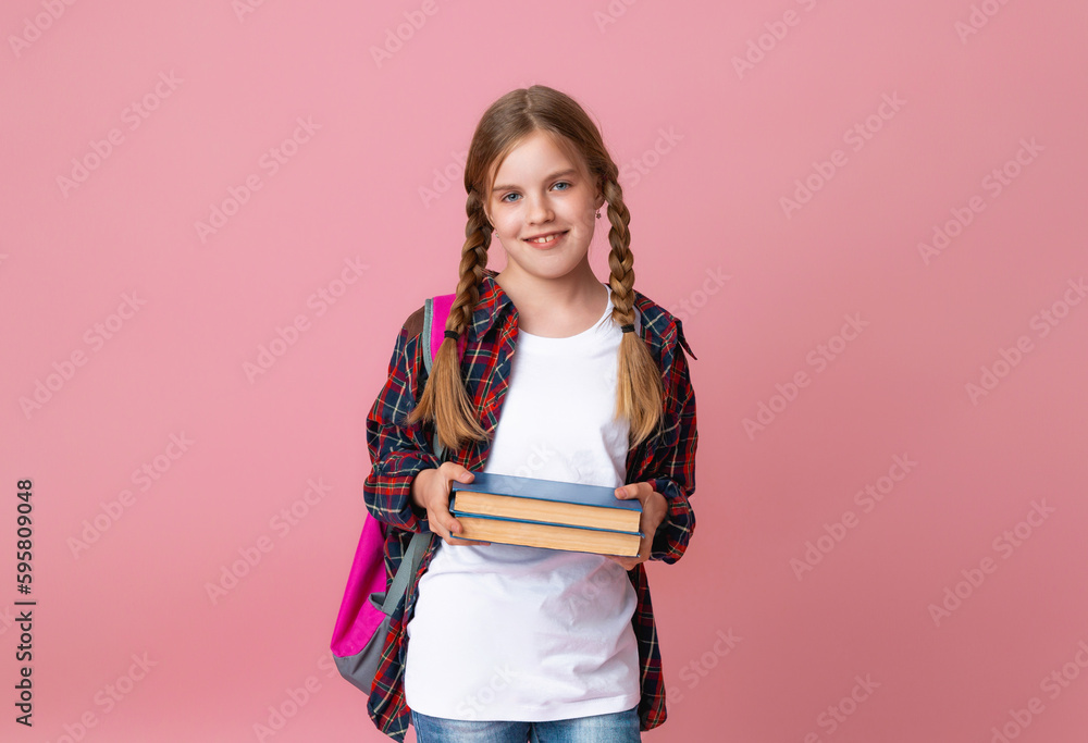 Smiling little blonde girl 10-12 years old in school uniform with backpack holding books isolated on pastel pink background studio portrait. The concept of children's lifestyle. Education at school. Smiling little blonde girl 10-12 years old in school uniform with backpack holding books isolated on pastel pink background studio portrait. The concept of children's lifestyle. Education at school.