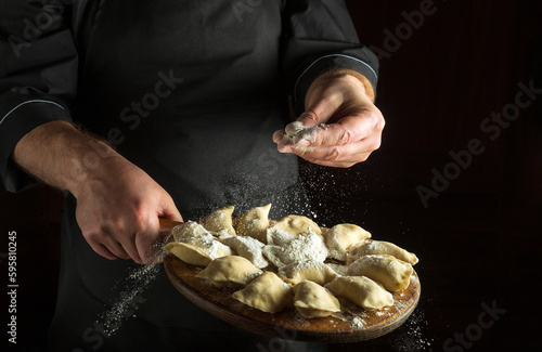 Professional chef throws flour to raw dumplings on a cutting kitchen board before cooking. Black space for menu or recipe