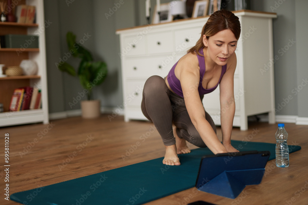 Beautiful woman with tablet computer watching workout video on yoga mat at home Beautiful woman with tablet computer watching workout video on yoga mat at home