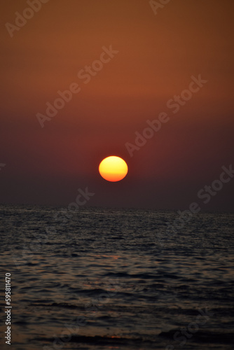 Fototapeta Naklejka Na Ścianę i Meble -  Vibrant sunset descending on the horizon, sea in golden colors, small waves gently touching the sands,
