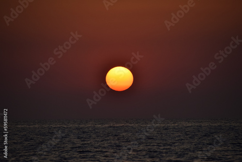 Vibrant sunset descending on the horizon, sea in golden colors, small waves gently touching the sands, © doda