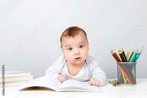 Baby reads a book, stack of books and pencils. Concept, teacher's day, child at school. Young scientist, professor, at work.