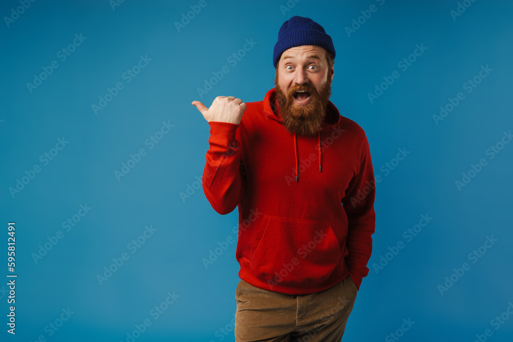 Naklejka premium Excited man pointing finger away at copy space isolated over blue background