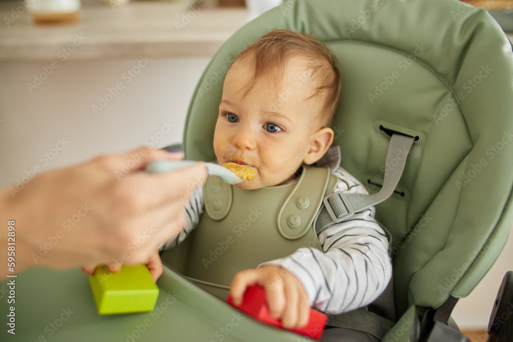 Mother spoon feeding her baby boy in the kitchen Mother spoon feeding her baby boy in the kitchen