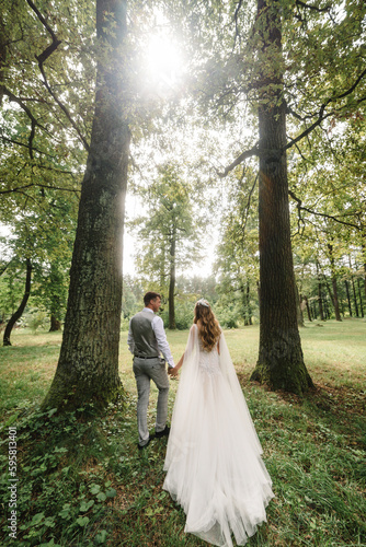 Portrait of young wedding couple are walking their backs in the forest and admire nature and look at the landscape. Wedding ceremony and photo shoot outdoors. Newlyweds. Rear view.