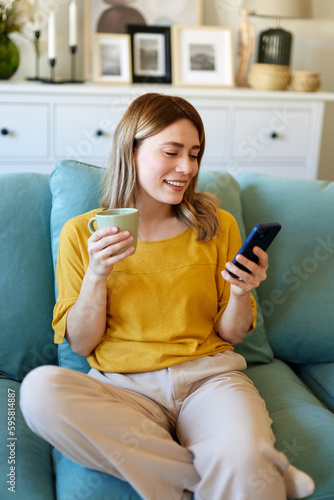 Woman using smartphone while drinking coffee at her home in the morning