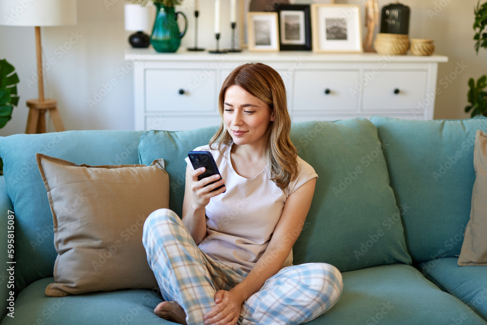 Happy woman text messaging on mobile phone while relaxing at home Happy woman text messaging on mobile phone while relaxing at home