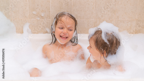 Funny sisters - baby girls playing with Soap Foam in the bath. Fun and children hygiene concept