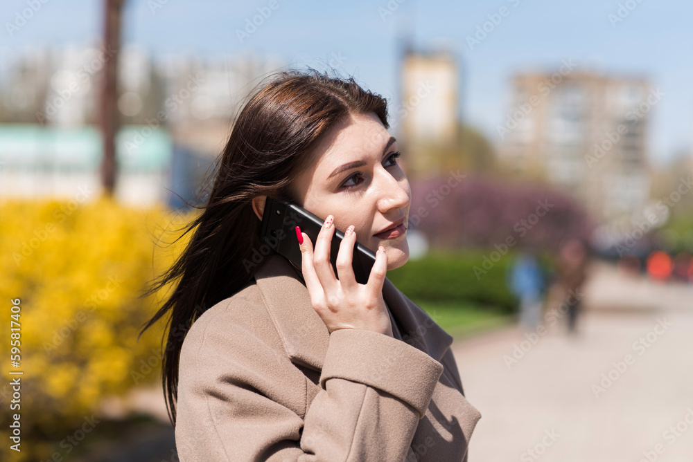 Caucasian brunette girl talking on a mobile phone while walking on the street in autumn or spring Caucasian brunette girl talking on a mobile phone while walking on the street in autumn or spring