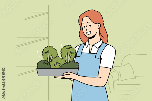 Smiling woman in apron holding box with greenery in hands. Happy girl with microgreen container work in greenhouse. Vector illustration. 