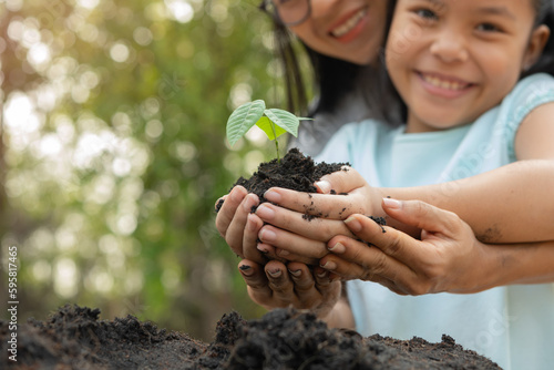hands holding young plant with soil.World environment day and sustainable environment concept. Mom and her child girl plant sapling tree. Teamwork protecting and reduce global warming earth.