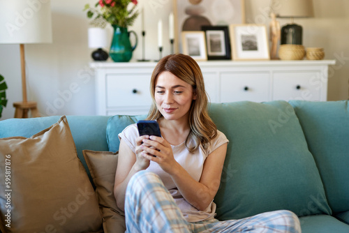 Happy woman text messaging on mobile phone while relaxing at home