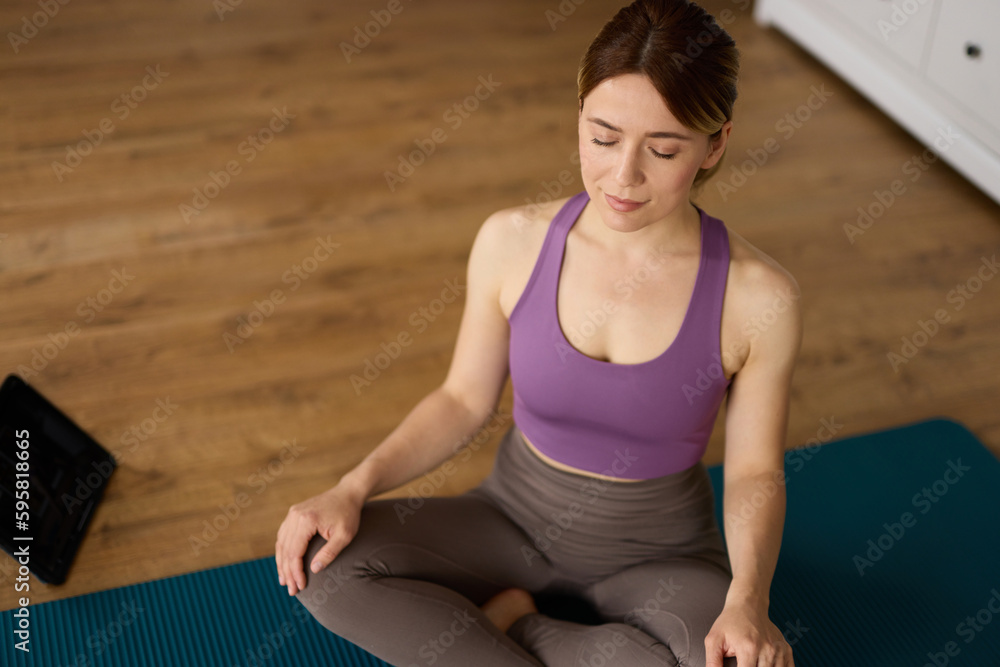 Young woman doing yoga and meditating at home while watching tutorial lessons on digital tablet Young woman doing yoga and meditating at home while watching tutorial lessons on digital tablet