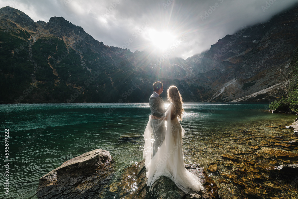 The bride and groom near the lake in the mountains. A couple together against the backdrop of a mountain landscape. Morskie Oko (Sea Eye) Lake. Tatra mountains in Poland. - obrazy, fototapety, plakaty 