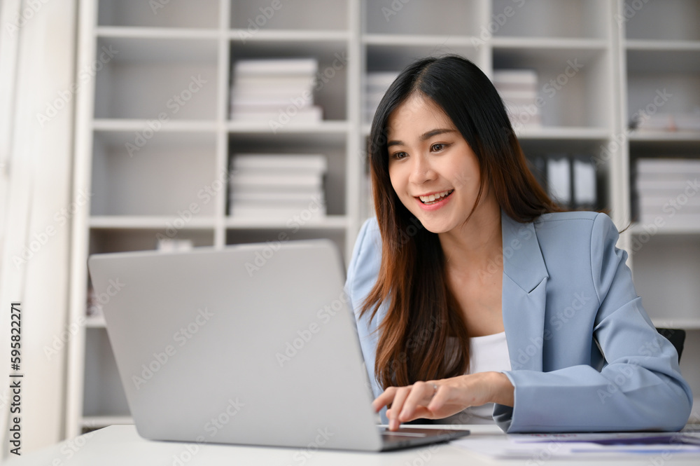 Smiling Asian businesswoman focusing on her business tasks on laptop, working in her office. Smiling Asian businesswoman focusing on her business tasks on laptop, working in her office.