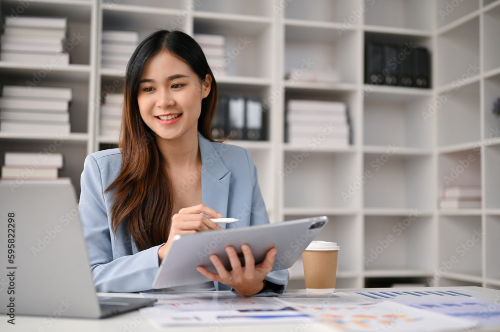 Attractive Asian businesswoman using her tablet and laptop at her desk Attractive Asian businesswoman using her tablet and laptop at her desk