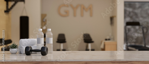 Copy space on a table with dumbbell  bottle of water  towel over blurred gym in the background.