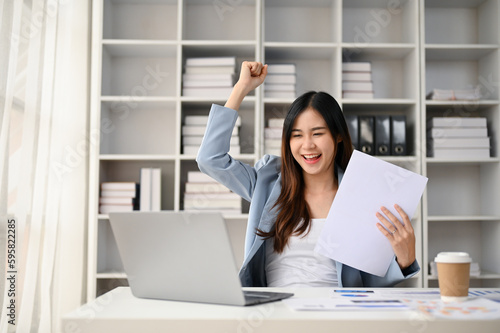 Cheerful Asian businesswoman rejoicing and celebrating her project success at her desk