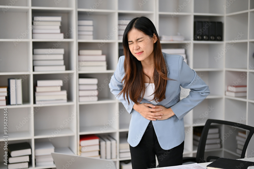 Sick Asian businesswoman suffering from stomachache or abdominal pain in her office. Sick Asian businesswoman suffering from stomachache or abdominal pain in her office.