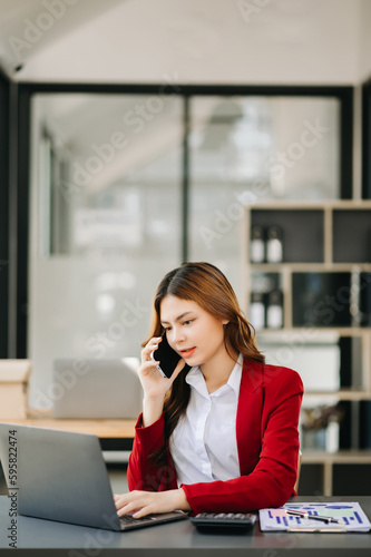 Business asian woman Talking on the phone and using a laptop with a smile while sitting at modern office.
