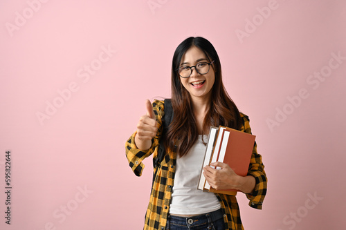Принти на полотні Cheerful Asian female college student with her schoolbooks showing thump up