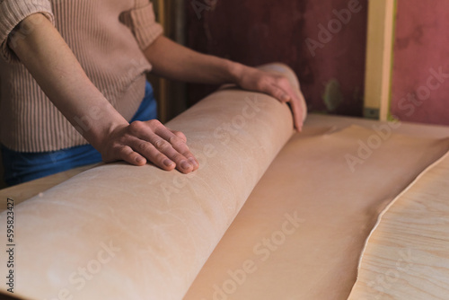 Foto accomplished woman leather crafter featuring a roll of superior leather in her atelier, underlining her expertise in working with only the best materials
