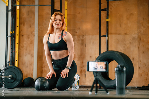 Smartphone is on the tripod, live stream, capturing video. Beautiful strong woman is in the gym