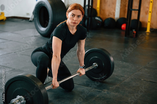 Leaning on the barbell. On the floor. Beautiful strong woman is in the gym