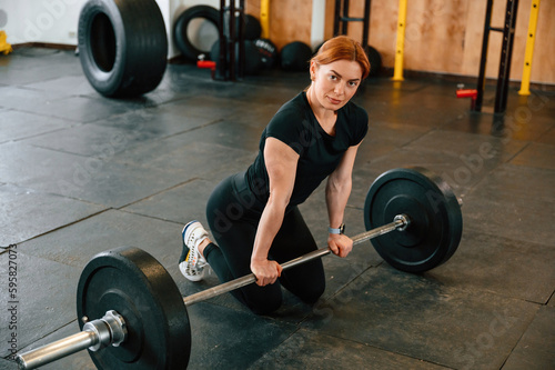 Leaning on the barbell. On the floor. Beautiful strong woman is in the gym