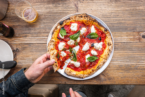 Wallpaper Mural Male hand taking a slice of pizza freshly baked Neapolitan Margherita Pizza on a rustic wooden table in a traditional Pizzeria. Torontodigital.ca