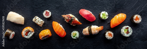 Sushi overhead flat lay panorama. Rolls, maki, nigiri on a black slate background, Japanese food. Salmon, eel, shrimp, tuna etc with rice, top panoramic shot