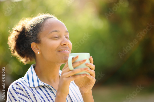 Obraz na płótnie Relaxed black woman smelling coffee in a park