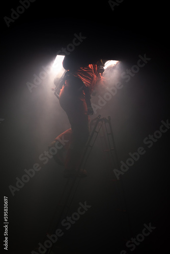 Vertical picture of firefighter is trying to climb a ladder to the top in the dark room with soft light.