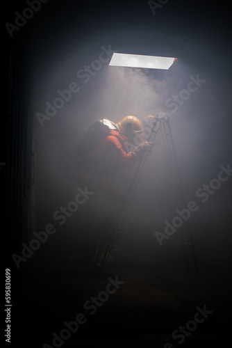 Vertical picture of firefighter is trying to climb a ladder in the dark room with soft light.