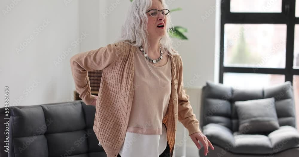Elderly woman suffering from lower back pain gets up from sofa. Back