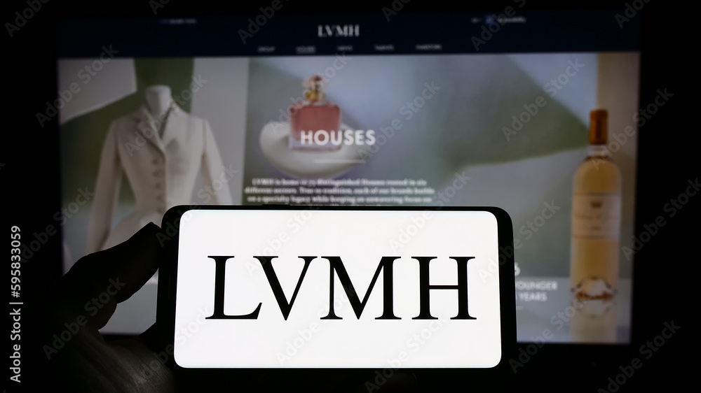 Stuttgart, Germany - 04-16-2023: Person holding smartphone with logo of  company LVMH Moet Hennessy Louis Vuitton SE on screen in front of website.  Focus on phone display. Stock Photo