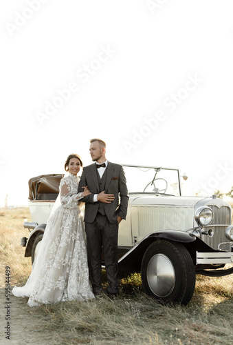 young groom circles the happy bride at sunset of the wedding day overlooking the sea. wedding couple with retro car. wedding gift