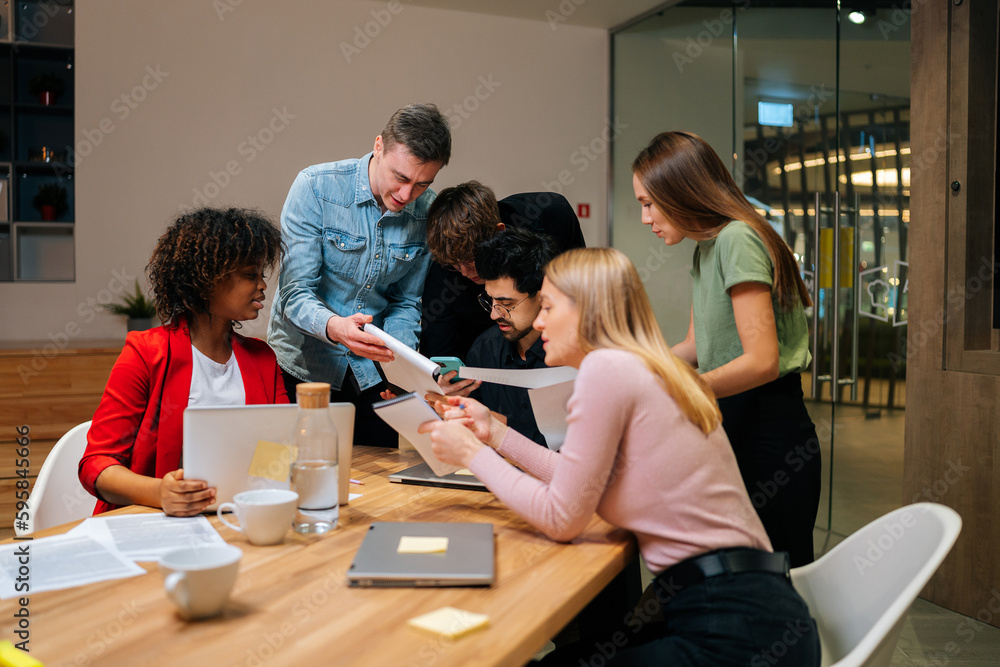 Diverse male and female employees working with project documents at meeting in boardroom, sitting at table, analyzing statistics, reading financial report. Colleagues engaged in teamwork at briefing Diverse male and female employees working with project documents at meeting in boardroom, sitting at table, analyzing statistics, reading financial report. Colleagues engaged in teamwork at briefing