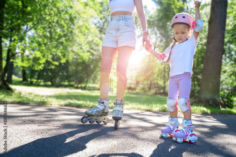 Mother teaching child daughter to skate on inline skates rollers in public park in summer. Family leisure outdoor sport activity game. Copy negative space