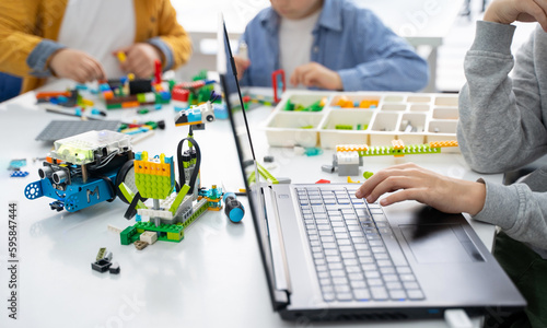 Robotics programming class. Children construct and code Robot. STEM education using constructor blocks and laptop, remote control joystick. Technology educational development for school kids. 