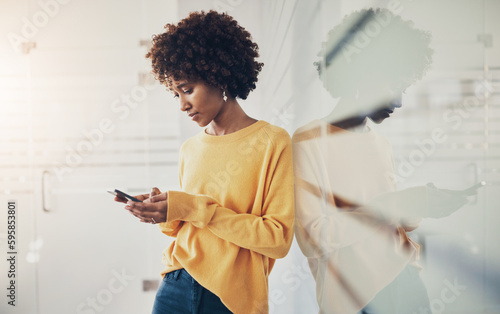 Young businesswoman leaning against a glass wall and texting on her mobile
