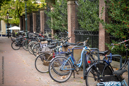 Lots of bikes are parked near the fence. Parking with bicycles on the street