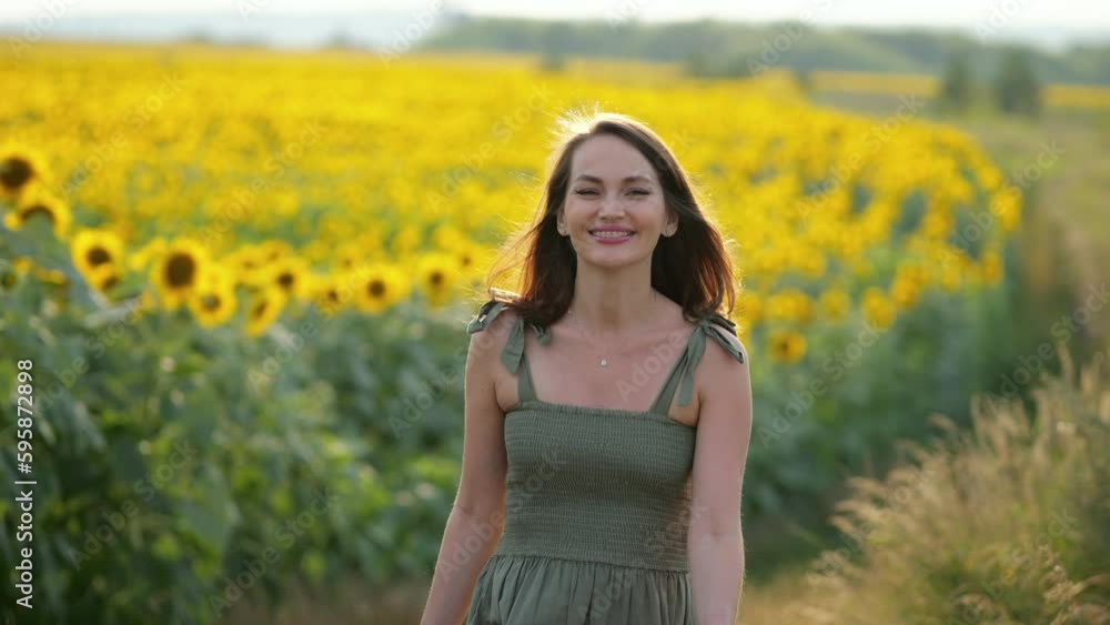Brown-haired woman walks past huge field of bright blooming sunflowers. Lady wearing green dress enjoys life spending weekends in countryside Brown-haired woman walks past huge field of bright blooming sunflowers. Lady wearing green dress enjoys life spending weekends in countryside