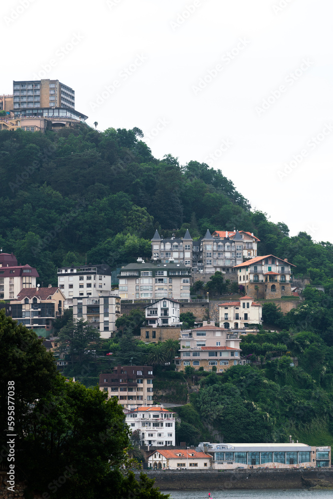 Naklejka premium SAN SEBASTIAN, Spain July 08 2022: View of Igeldo Mountain. Beautiful urbanisation with sensational view all over the La Concha Bay. Igeldoko Dorrea tower in left corner. Vertical photo.