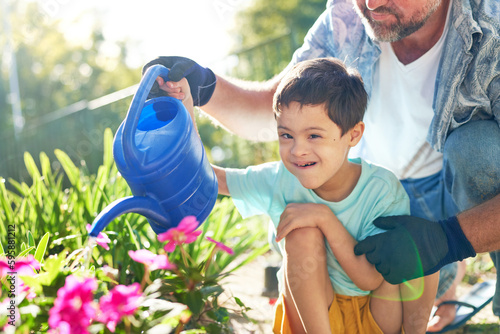 Portrait happy boy with Down Syndrome watering flowers with father photo